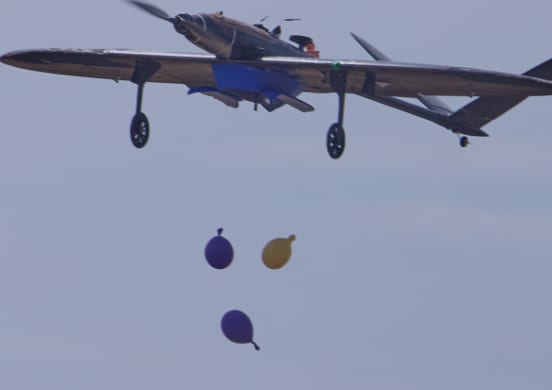 A fixed-wing aircraft dropping payloads over the field at AeroCup